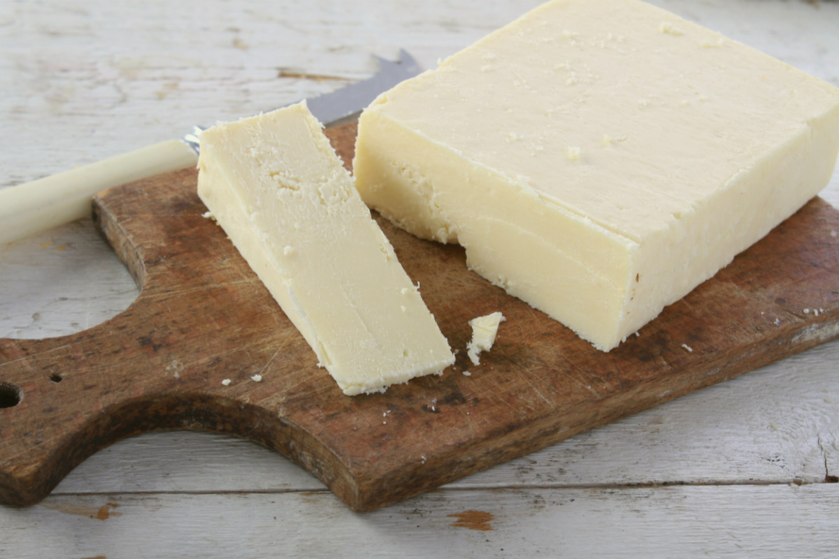 A block and small wedge of Cheshire cheese are on a cutting board. There is a knife next to it. | Girl Meets Food