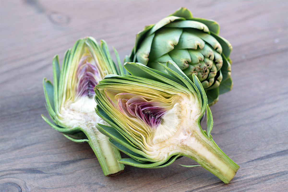 An artichoke heart and two halves are on a wooden surface | Girl Meets Food