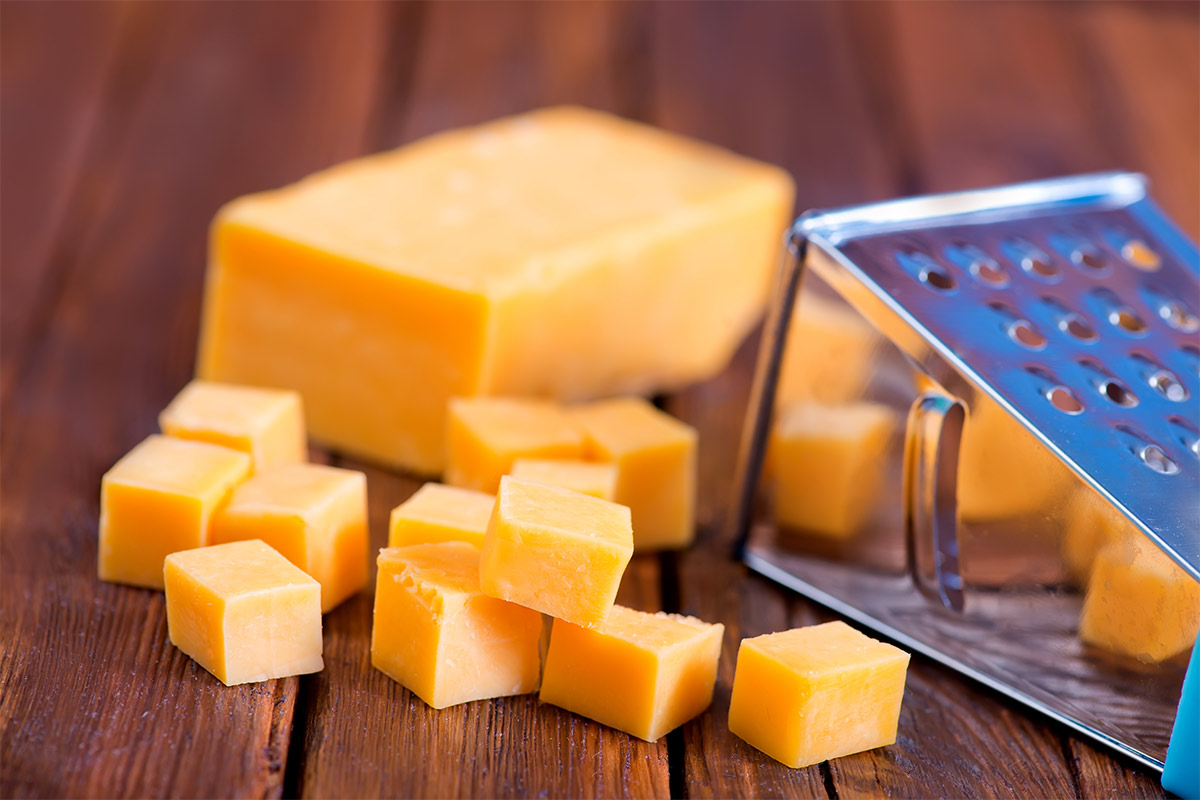 Cheddar cubes on a wooden surface with grater | Girl Meets Food