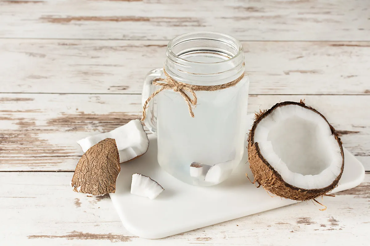 A glass of coconut water and a few pieces of coconut are on a white cutting board | Girl Meets Food