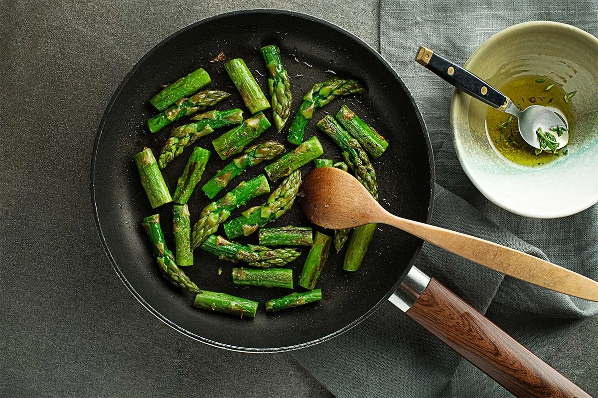 Cooked asparagus is in the pan. There is a white bowl with an oil next to it.  | Girl Meets Food