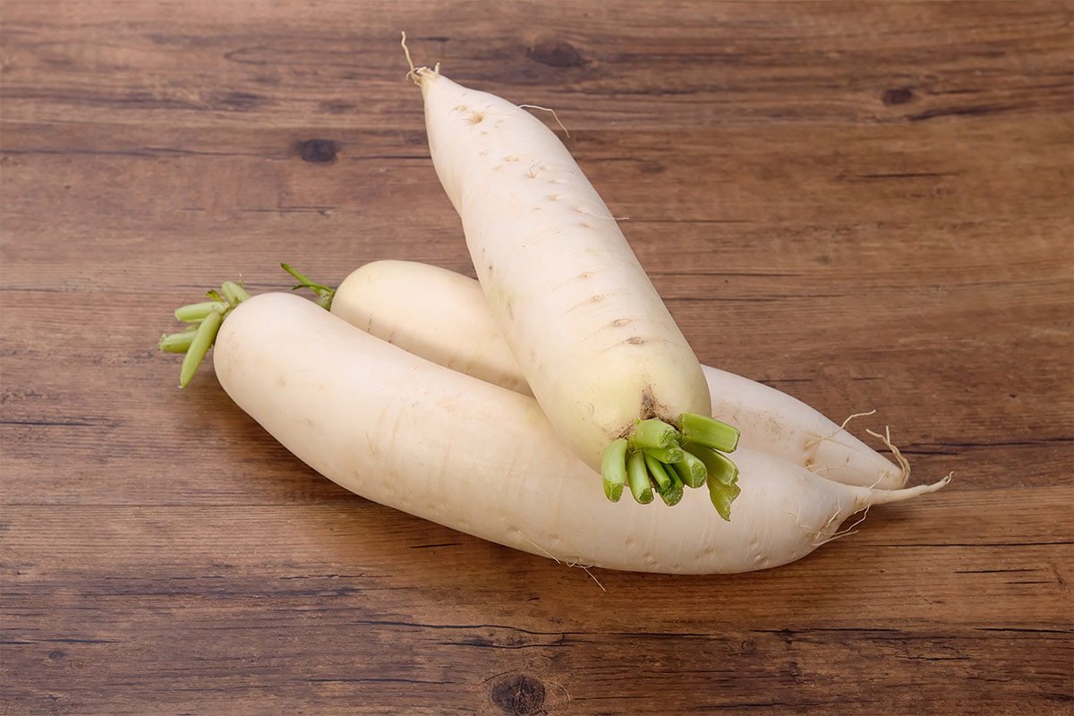 Three daikon radishes are on a wooden background | Girl Meets Food