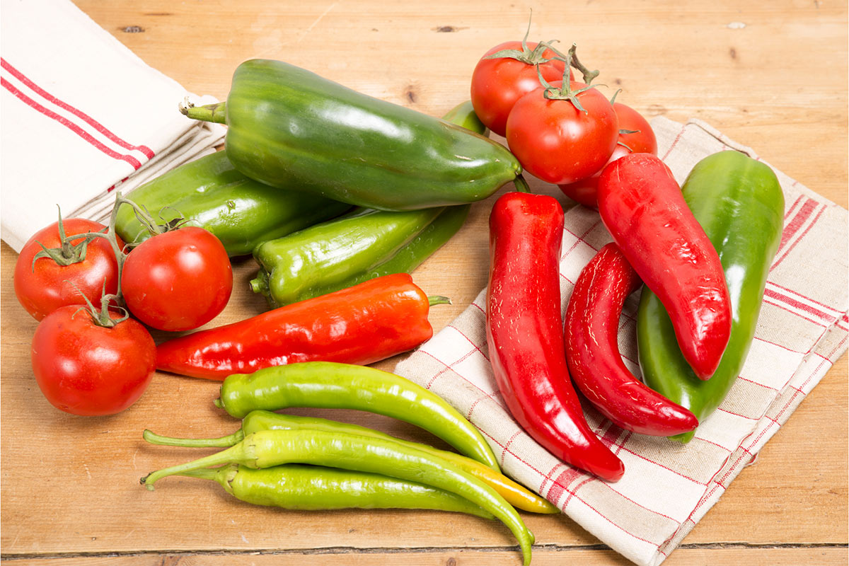 Assorted peppers and tomatoes are laid on a napkin and wooden surface | Girl Meets Food