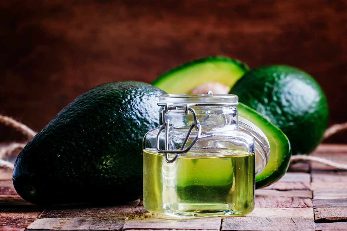 A jar of avocado oil stands on a wooden surface. There are some avocados next to it | Girl Meets Food