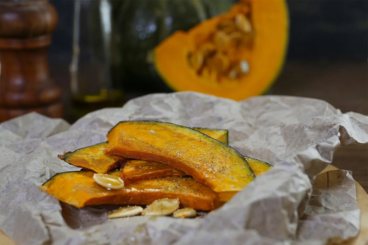 Baked kabocha squash slices with some seeds lie on a parchment paper | Girl Meets Food