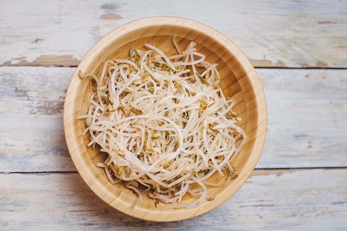 A wooden bowl of fresh bean sprouts stands on a wooden surface | Girl Meets Food