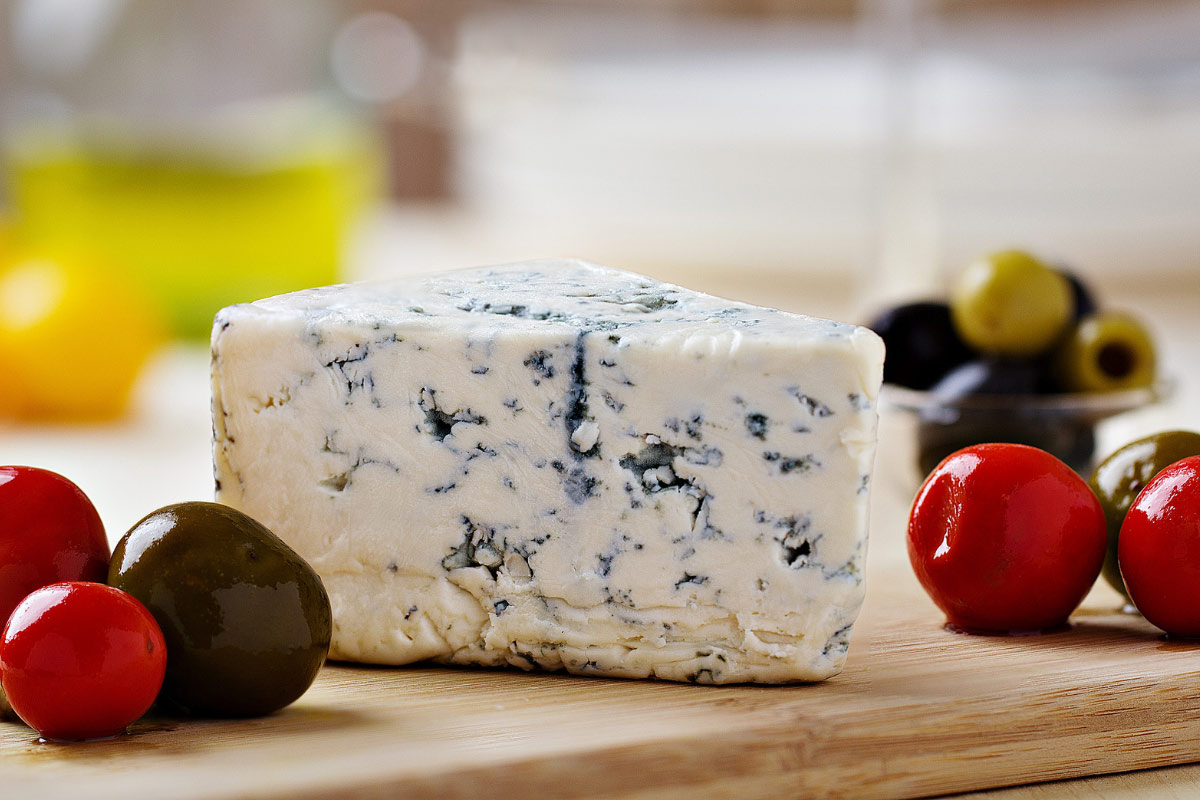 A wedge of blue cheese and a few tomatoes are on a cutting board. | Girl Meets Food