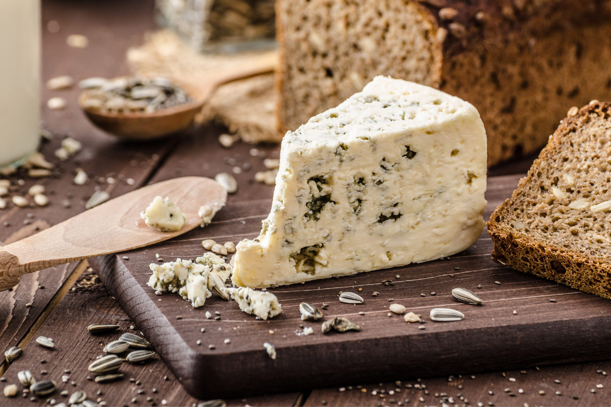 A piece of blue cheese, whole grain bread and a wooden knife are on a wooden board. | Girl Meets Food