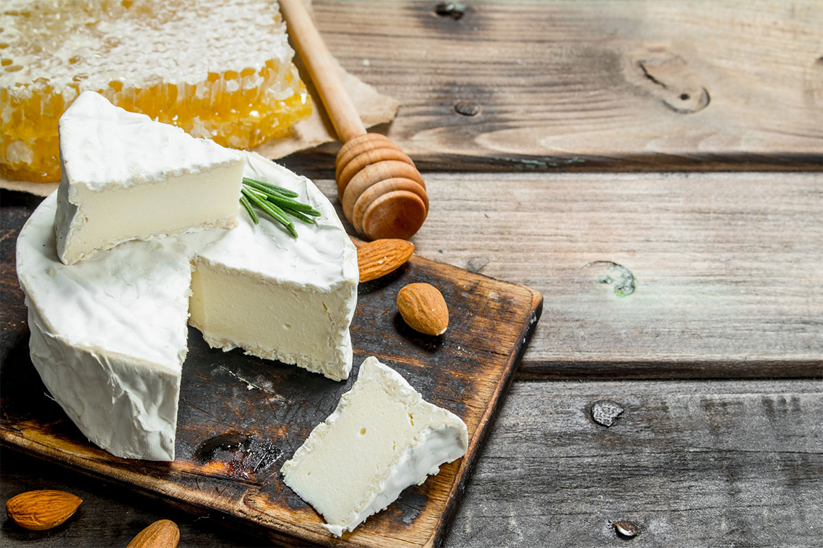 A block of brie with two almonds lie on a cutting board. There is honey next next to it | Girl Meets Food