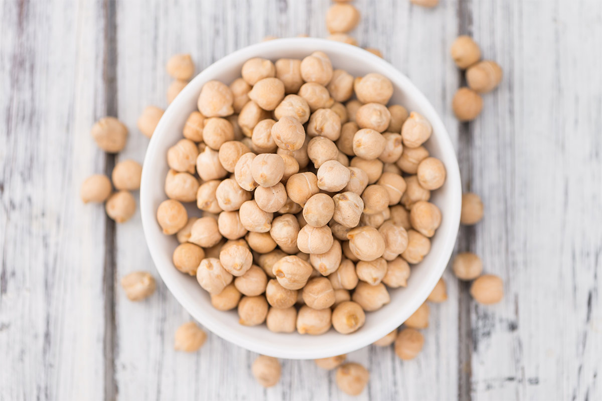 A white bowl of raw chickpeas stands on a white surface | Girl Meets Food