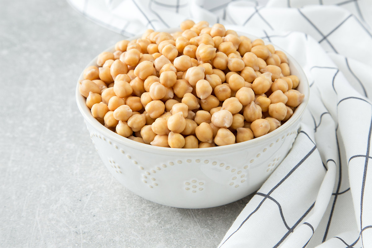 A white bowl of cooked chickpeas stands on a white surface. There is a white tablecloth next to it | Girl Meets Food