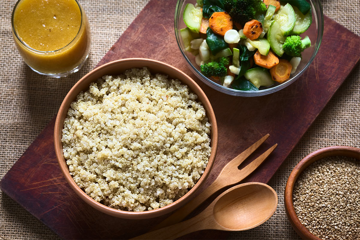 A bowl of cooked quinoa and a bowl of vegetables stand on a wooden board | Girl Meets Food