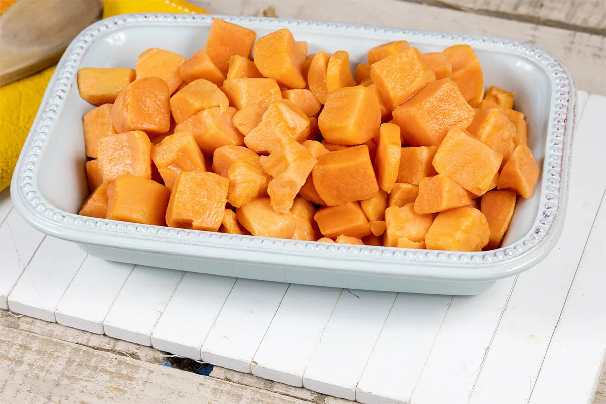 Raw sweet potatoes cubes are in a white baking dish that is on a white wooden surface | Girl Meets Food
