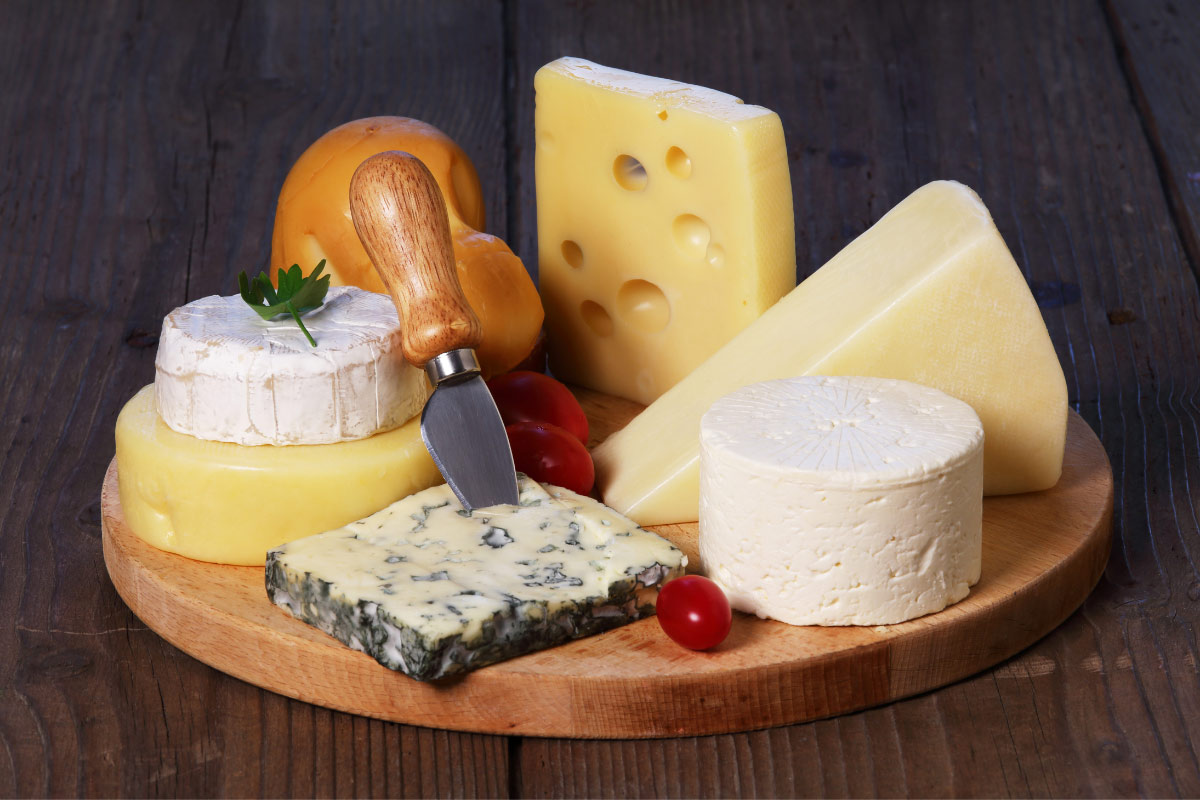 Different kinds of cheese are assembled on a round cutting board. | Girl Meets Food