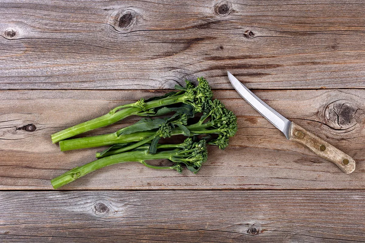 A bunch of Chinese broccoli and a knife lie on a wooden surface | Girl Meets Food