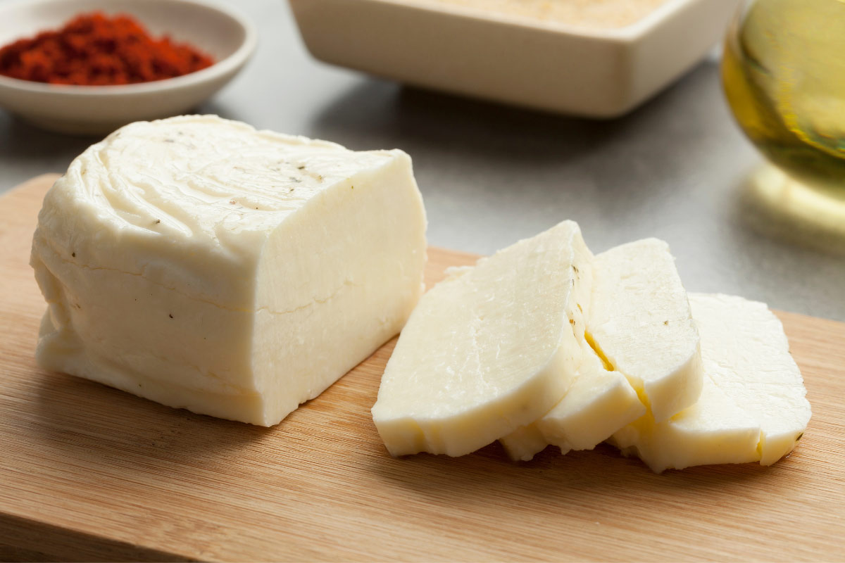 A piece of halloumi and 3 slices are on a wooden board. There are a few bowls on the background | Girl Meets Food