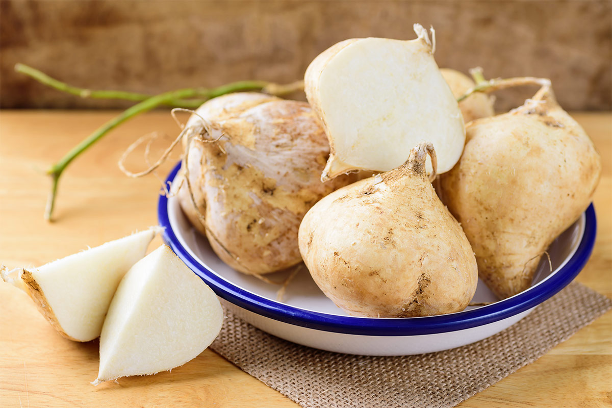 A few jicama vegetables are in a bowl that is on a wooden surface | Girl Meets Food