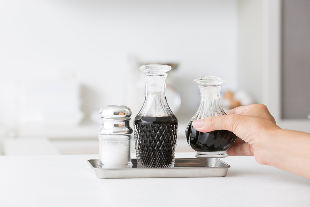 A woman's hand holds a bottle of soy sauce. There is another bottle and salt shaker next to it | Girl Meets Food
