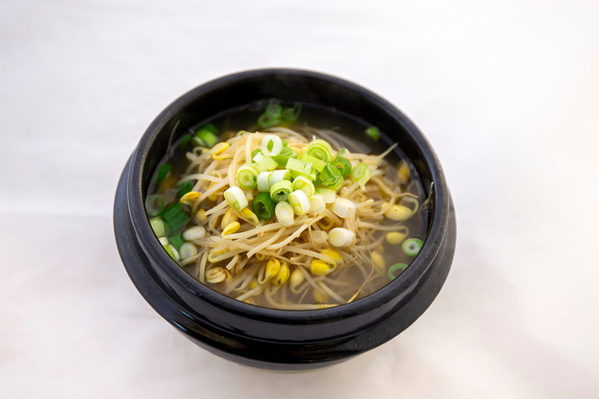 A black bowl of Korean bean sprout soup stands on a white surface | Girl Meets Food