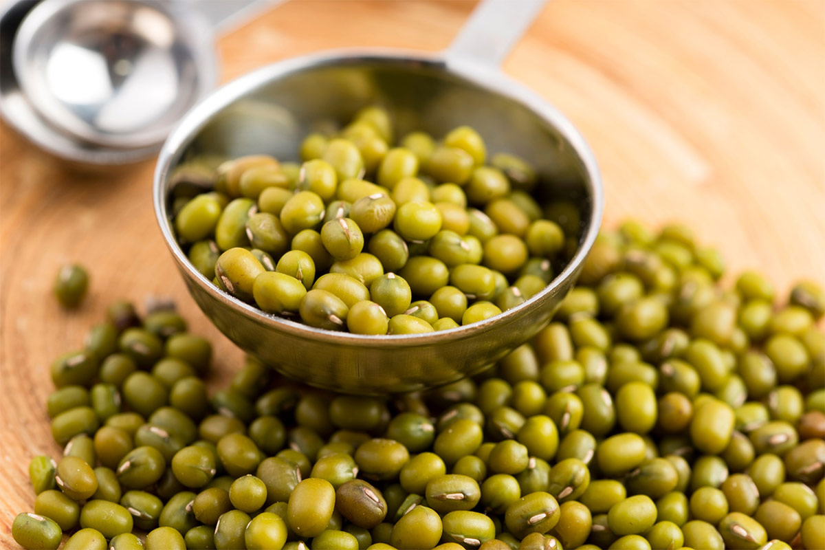 A metal scoop full of mung beans stands on a wooden board. There is another metal scoop and some mung beans scattered next to it | Girl Meets Food