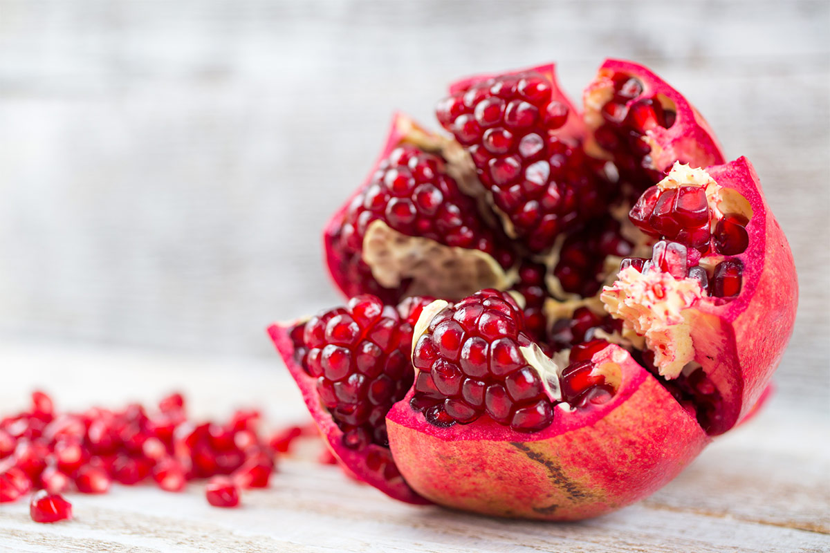 A cut pomegranates lies on a wooden surface | Girl Meets Food