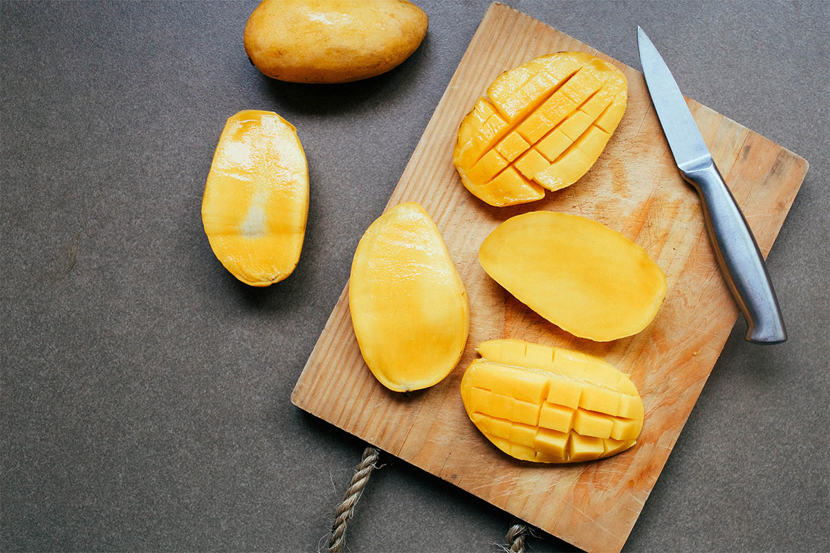 A few slices of mango are on a cutting board and grey surface | Girl Meets Food