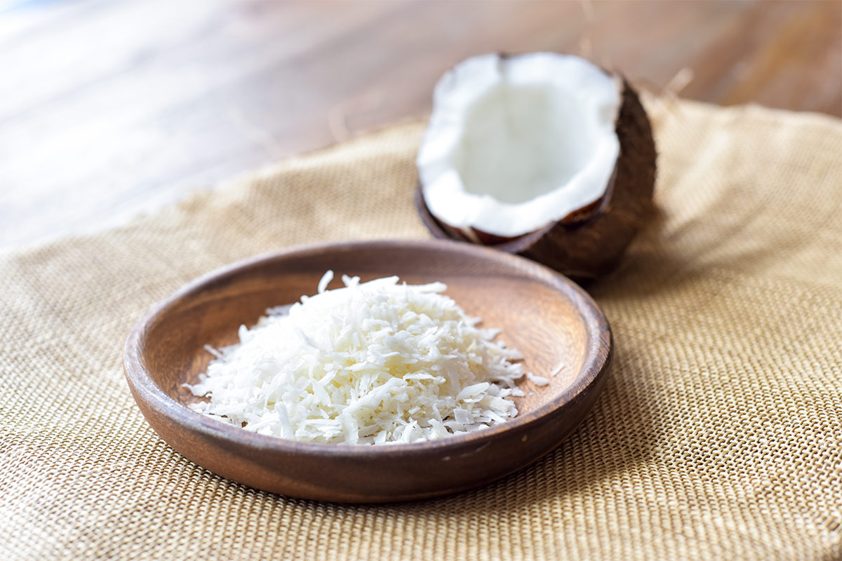 A wooden plate of shredded coconut and a half of coconut stand on a linen cloth | Girl Meets Food