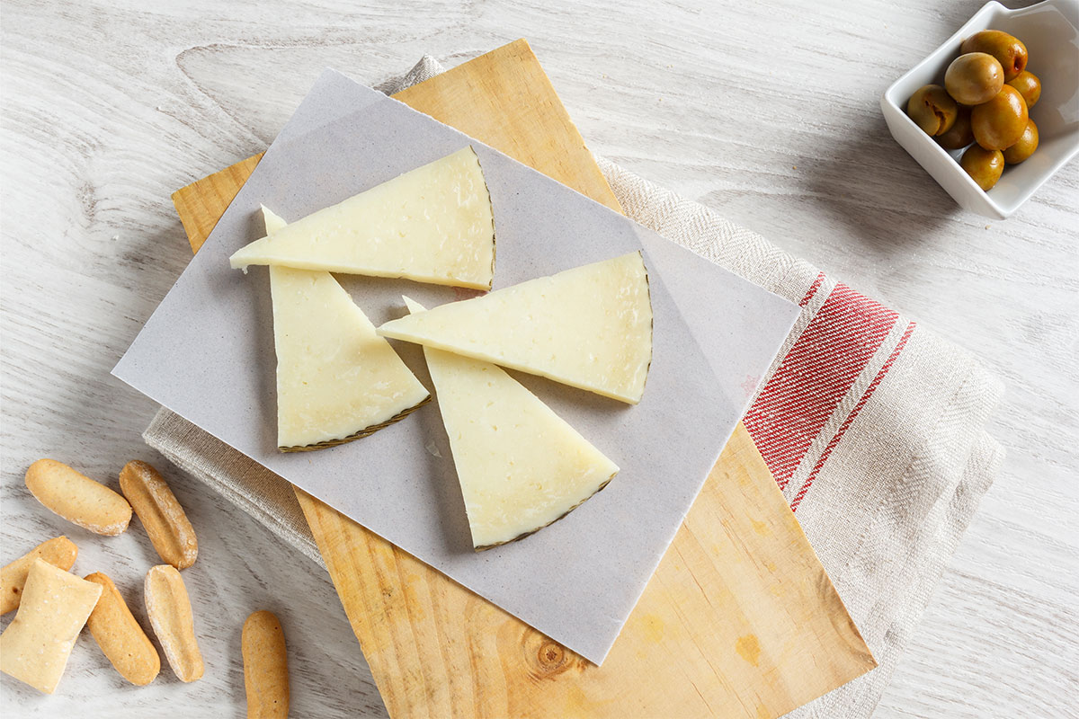 Four Manchego cheese slices on grey surface. There are olives and bread pieces around it | Girl Meets Food