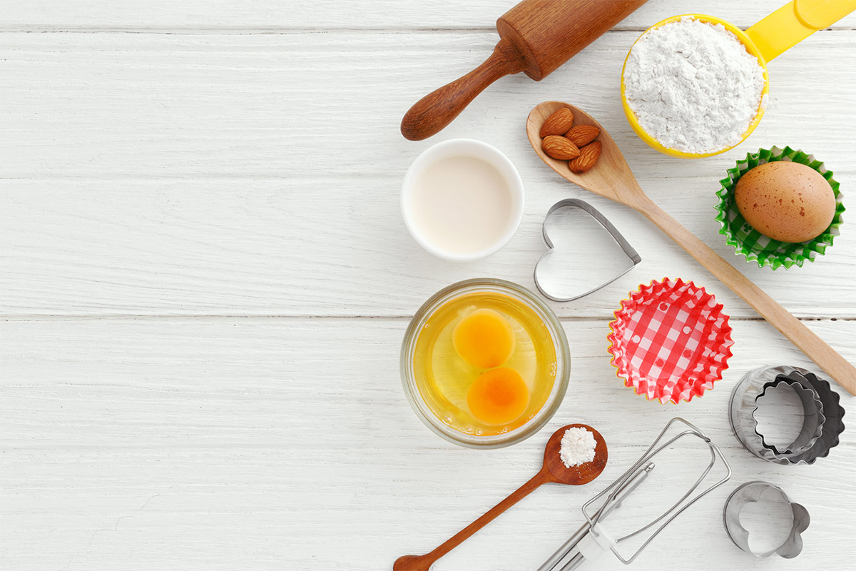 Baking ingredients like eggs, milk, almonds and some kitchen utensils for baking are on a white background | Girl Meets Food