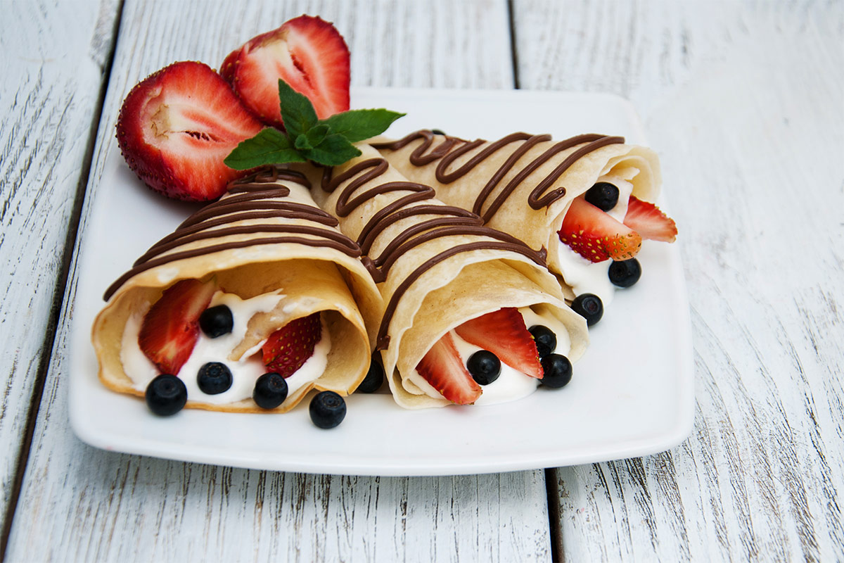 A white square plate with crepes and strawberries on a white wooden surface | Girl Meets Food