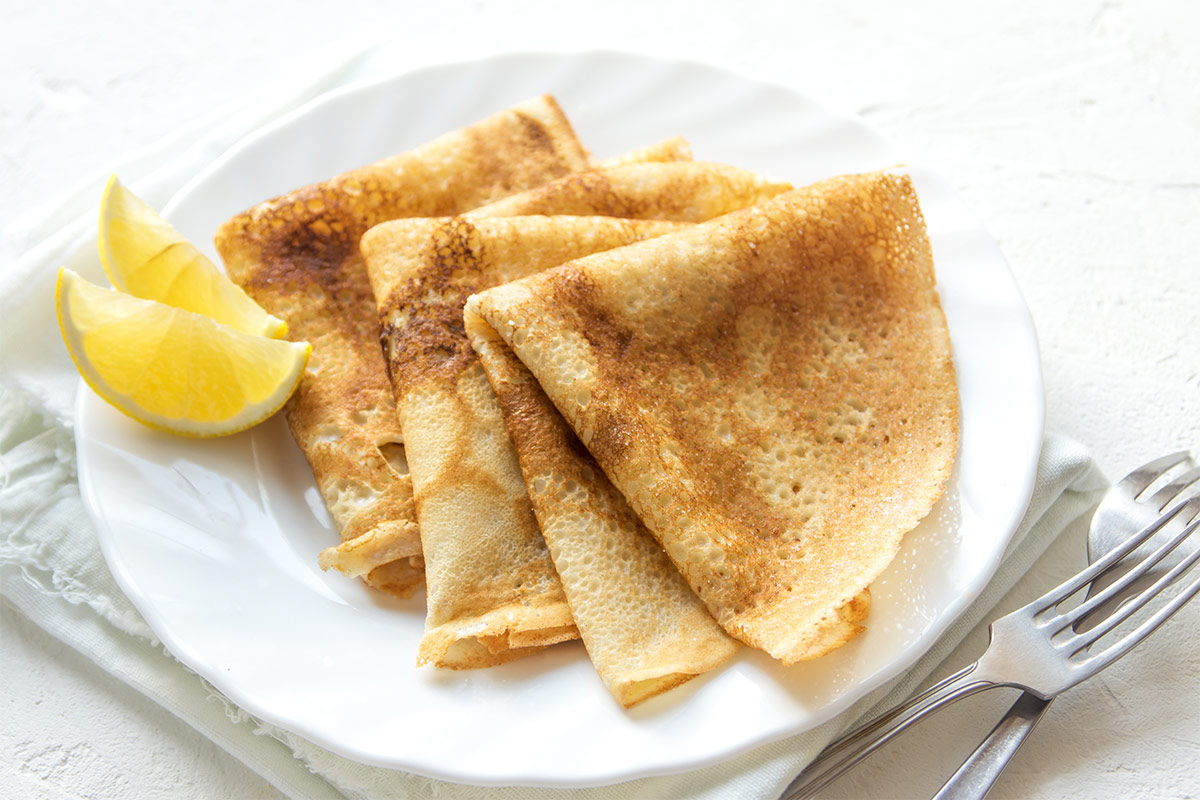 A white plate with crepes and lemon wedges is on a white surface. There are two forks next to the plate | Girl Meets Food