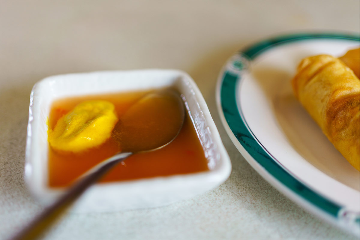 A small bowl with sauce and table spoon it is next to the plate of egg rolls | Girl Meets Food