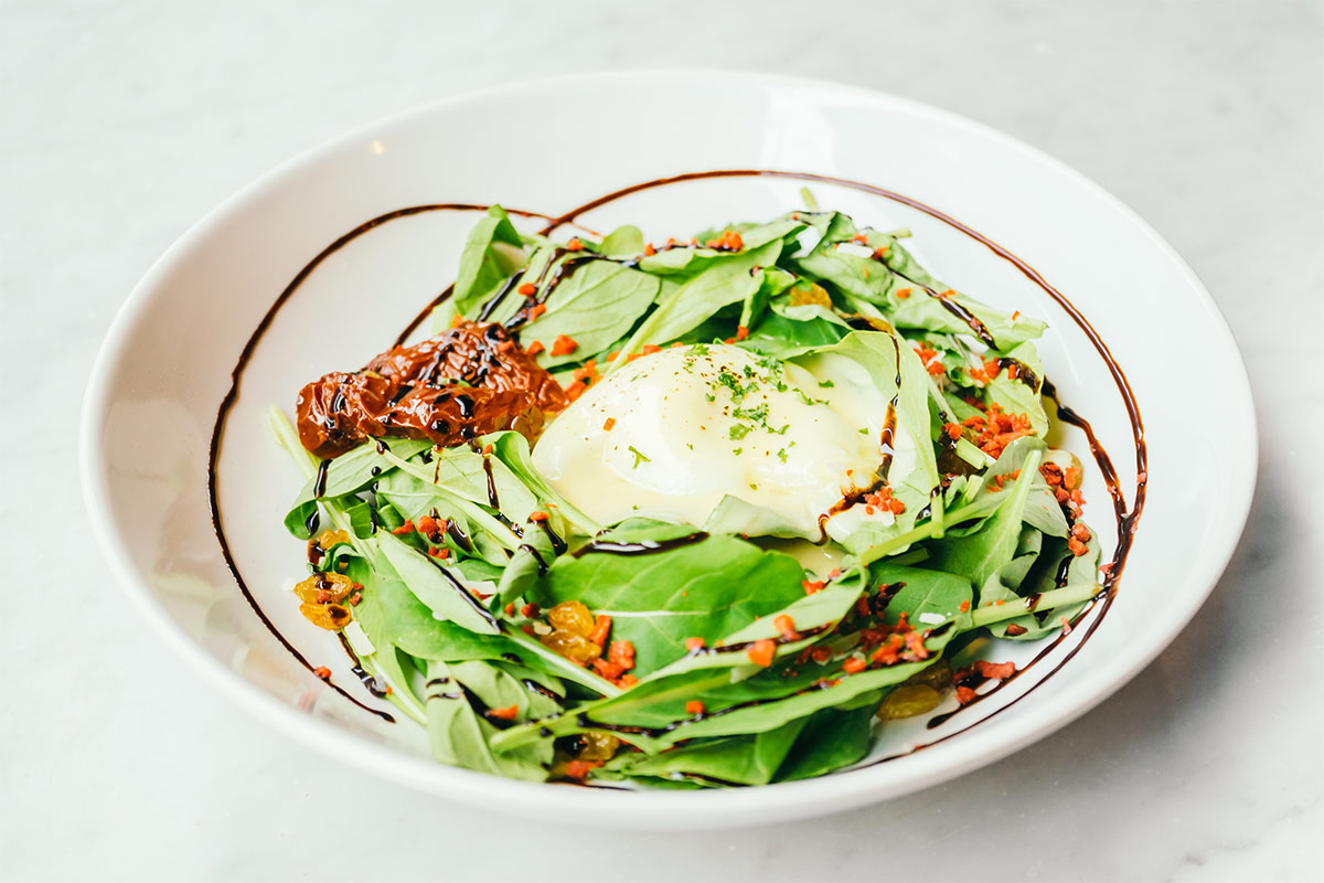 A bowl of eggs Benedict with salad is on a white surface | Girl Meets Food