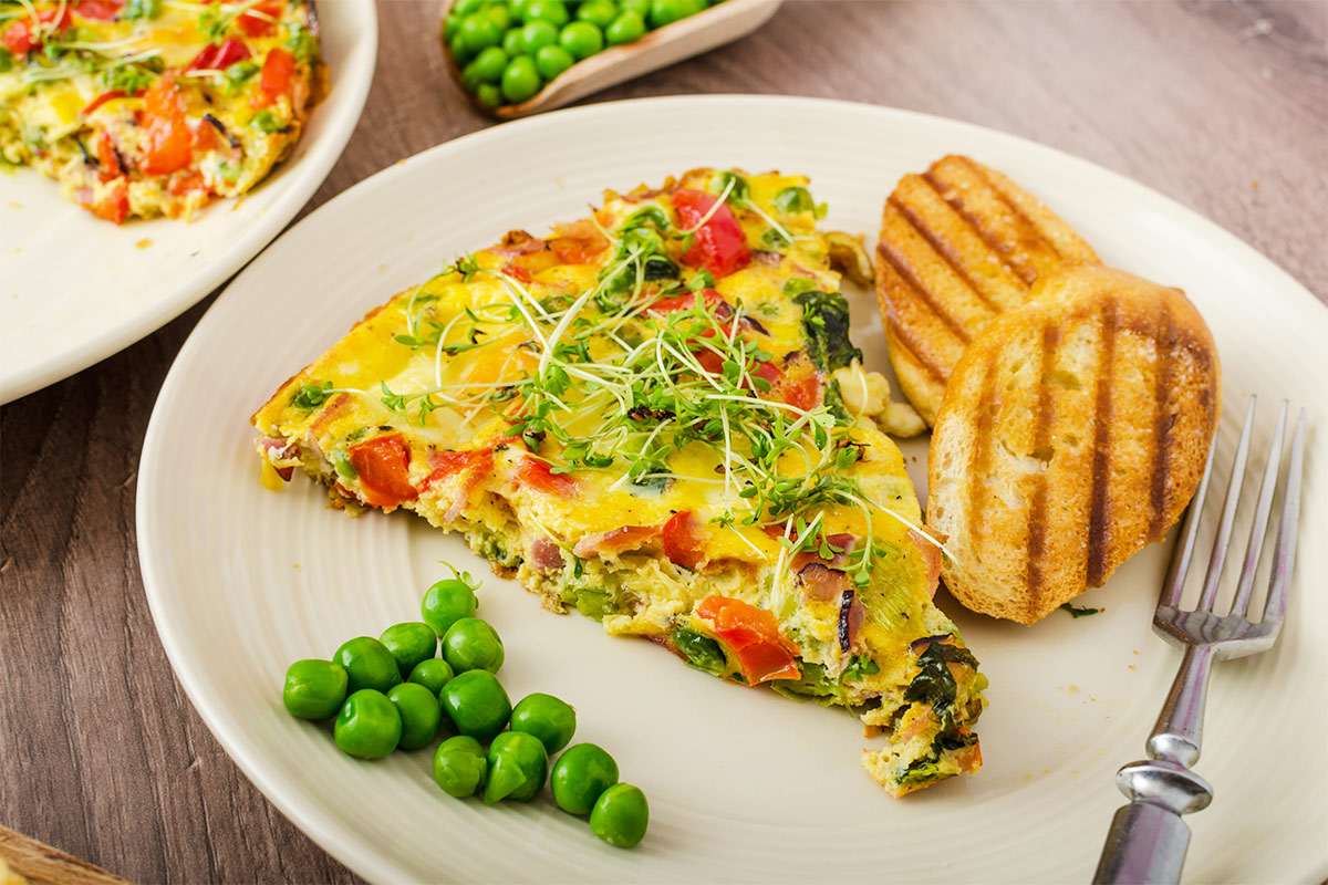A plate with a piece of frittata, some peas, 2 toasts and a fork is on the table | Girl Meets Food