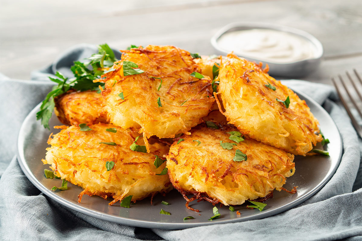 A plate of hash brown lie on a grey cloth. There is a fork and sour cream on a side | Girl Meets Food