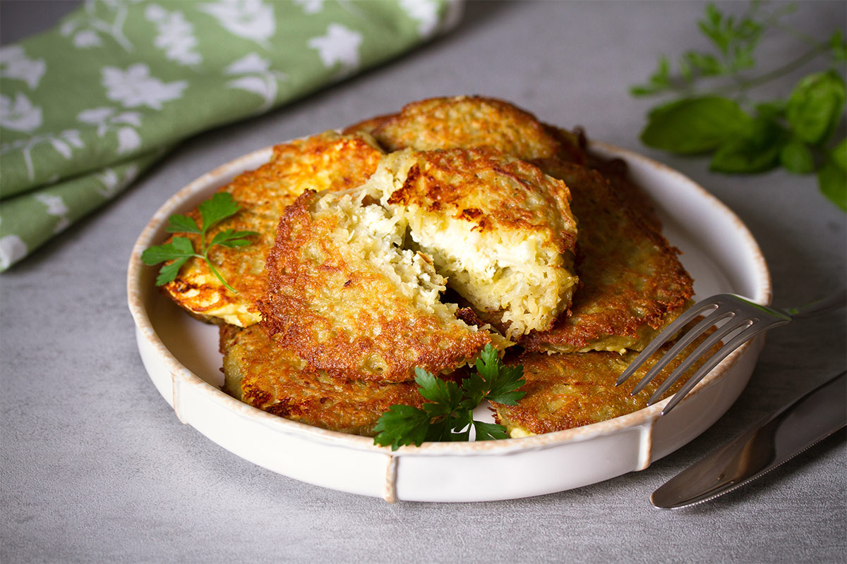 A round plate of hash brown is on the table. Next to it, there are some greens, fork and knife, a towel | Girl Meets Food