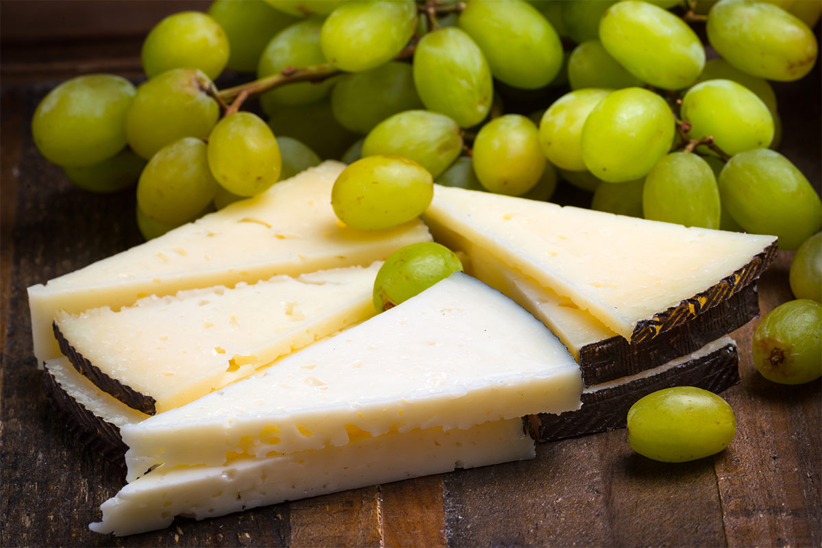 Manchego cheese slices with grapes on wooden surface | Girl Meets Food