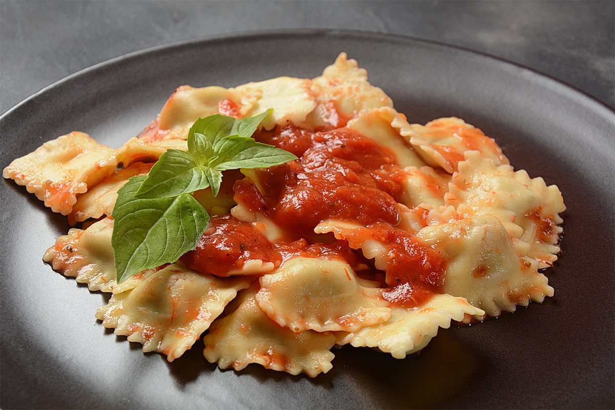 A black plate of ravioli topped with tomato sauce and basil leaves | Girl Meets Food