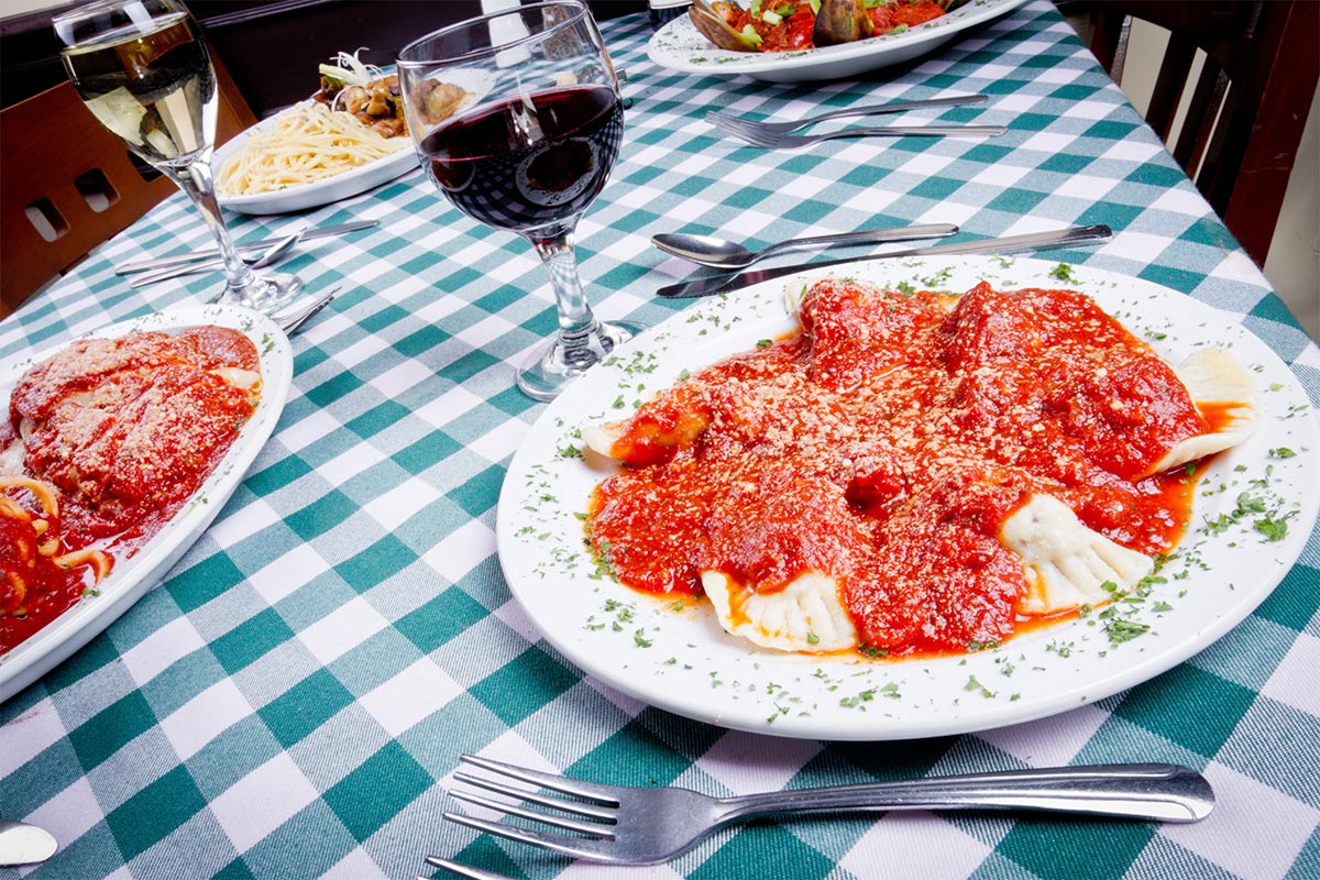 A table covered with a checkered tablecloth, served with plates of ravioli and glasses of wine | Girl Meets Food