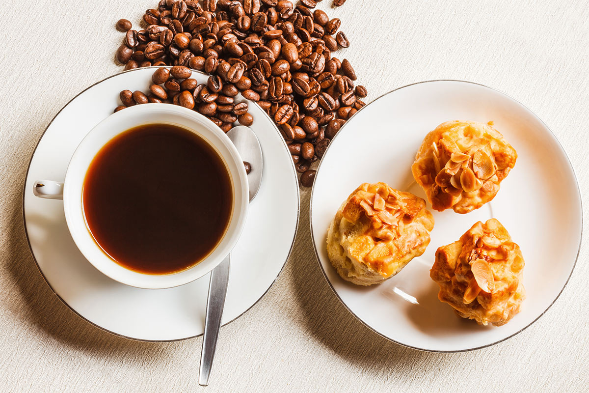 A plate with three scones, a cup of coffee and coffee beans scattered alongside it are on a white surface | Girl Meets Food