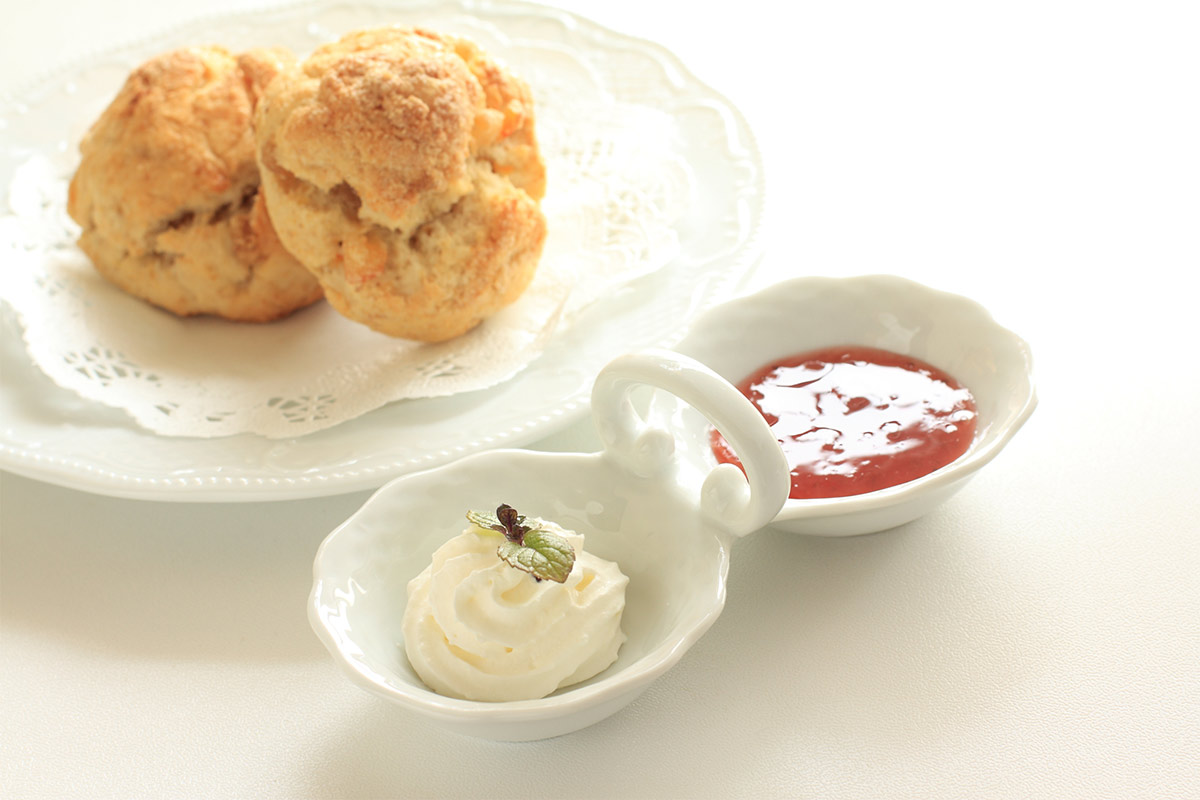 A plate with scones, a small bowl with cream and a small bowl with jam are on a white tablecloth | Girl Meets Food