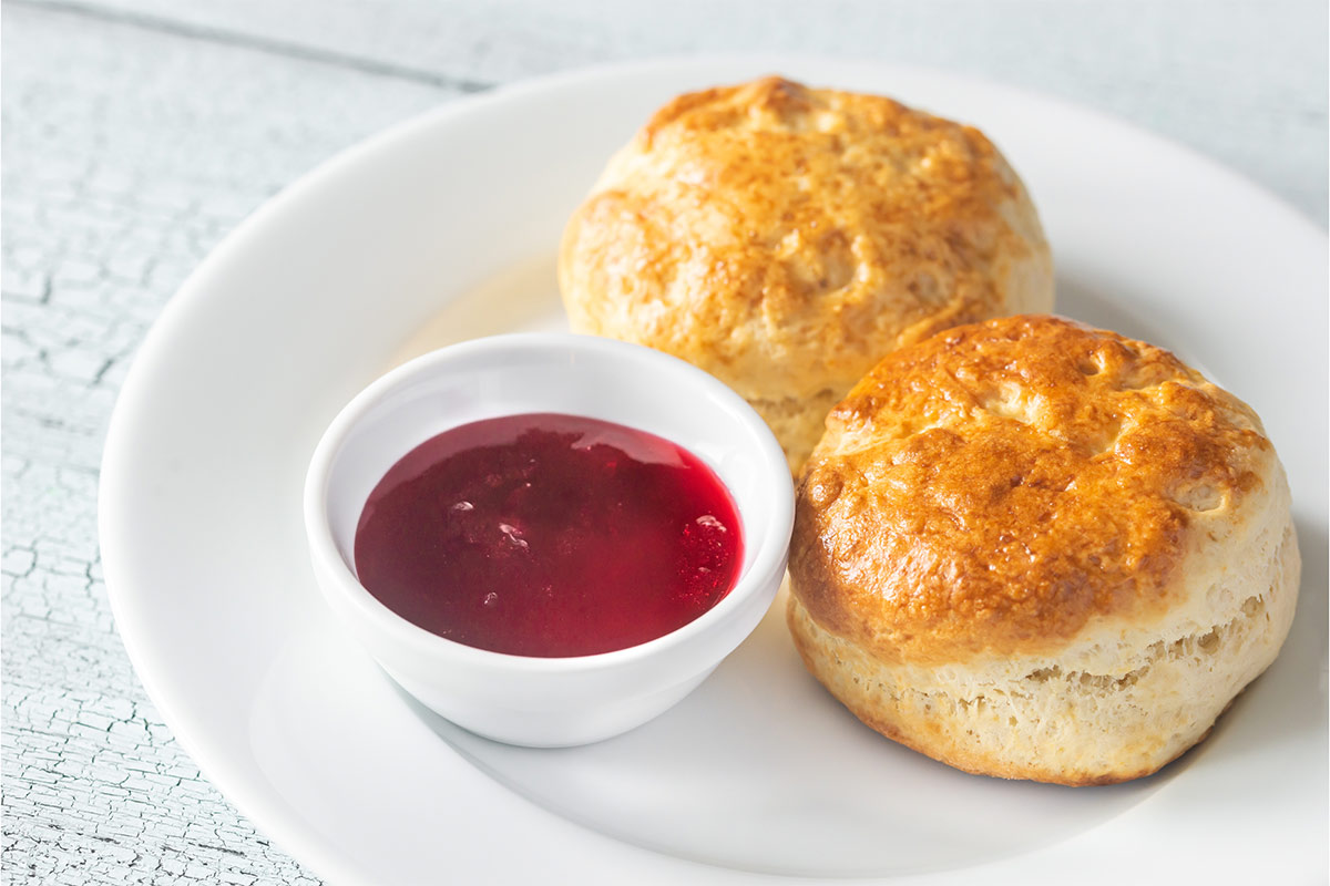 A plate with 2 scones and jam is on a white surface | Girl Meets Food