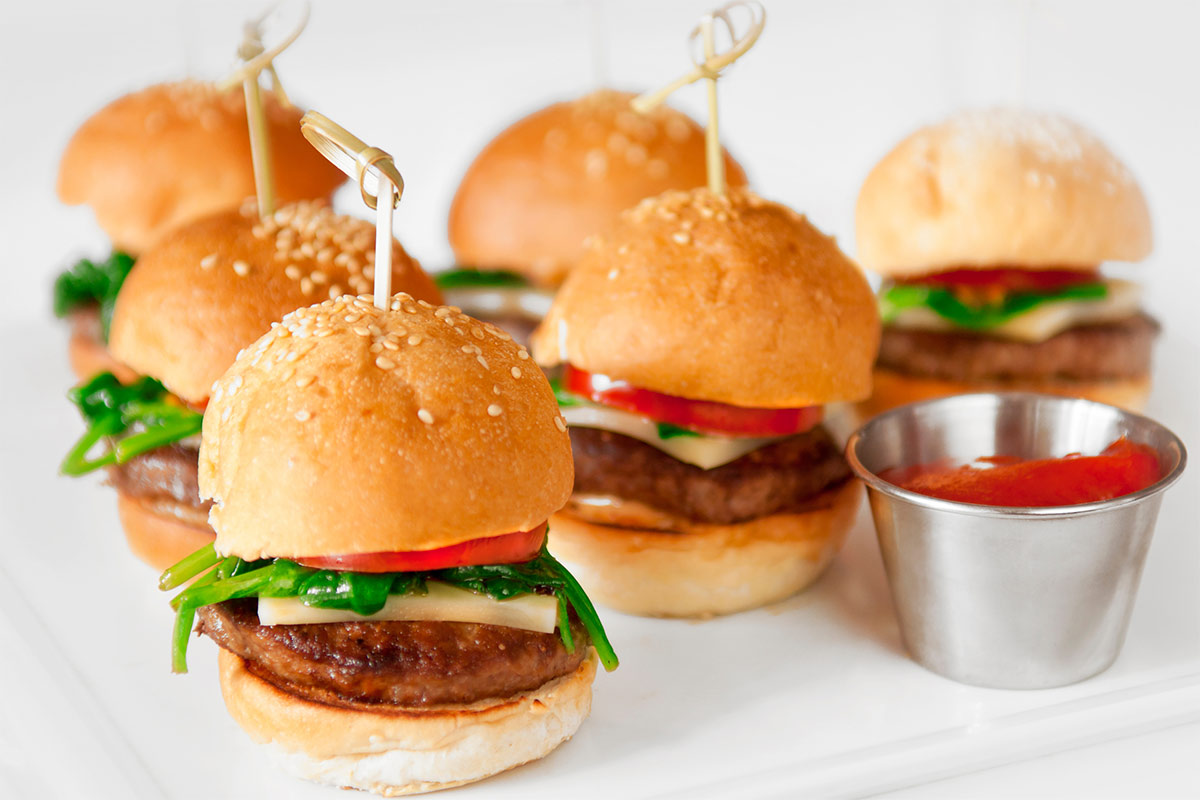 Several sliders and a tomato dip in a metal remakin are on a white surface | Girl Meets Food