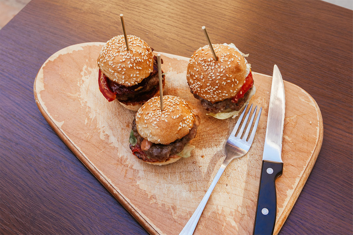 Three sliders, a fork and a knife are on a cutting board | Girl Meets Food