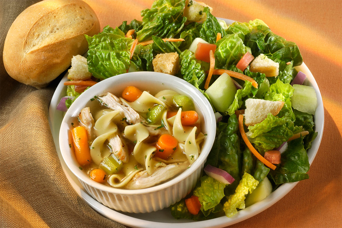 A bowl of minestrone soup and salad are on a plate. There is a bun next to it | Girl Meets Food
