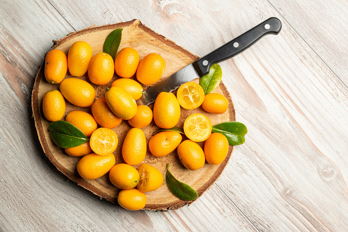 Nagami kumquat fruit with green leaves and a knife on a wooden board | Girl Meets Food