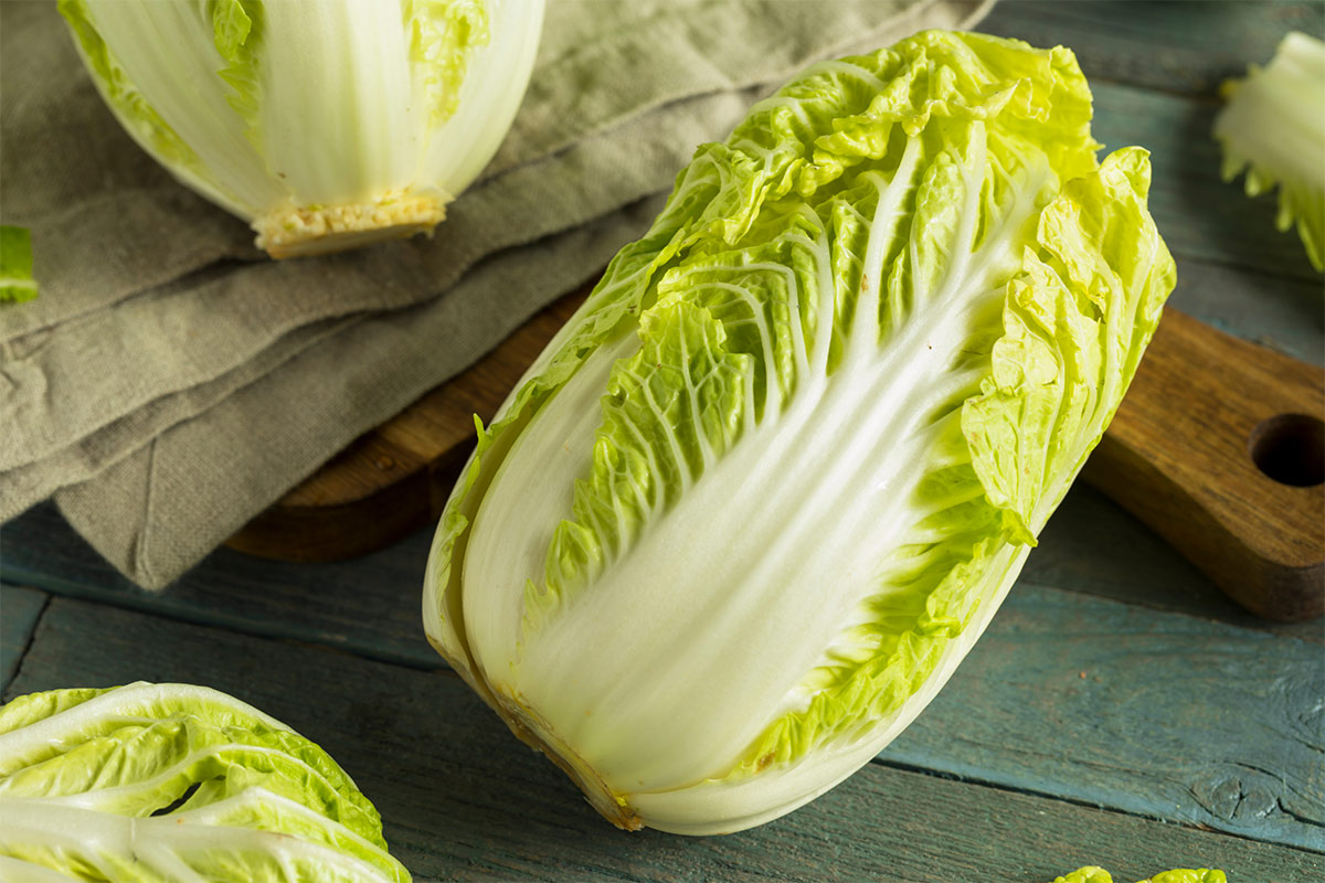 Several napa cabbages are on a wooden surface with chopping board and linen tablecloth | Girl Meets Food