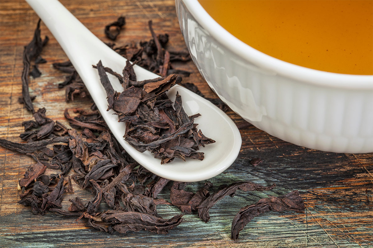 Oolong black tea is in a white ceramic teaspoon and on a table. There is also a white cup of tea | Girl Meets Food