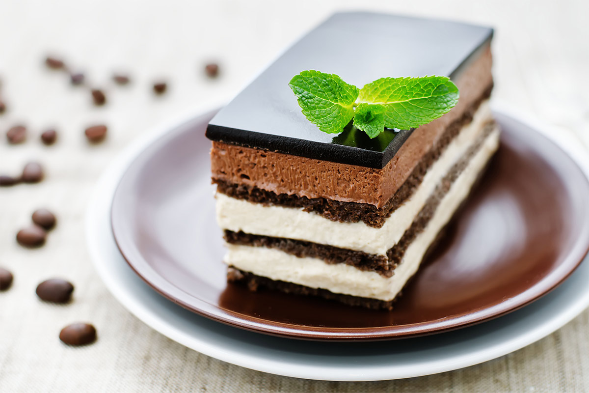 A piece of opera cake on a black plate | Girl Meets Food