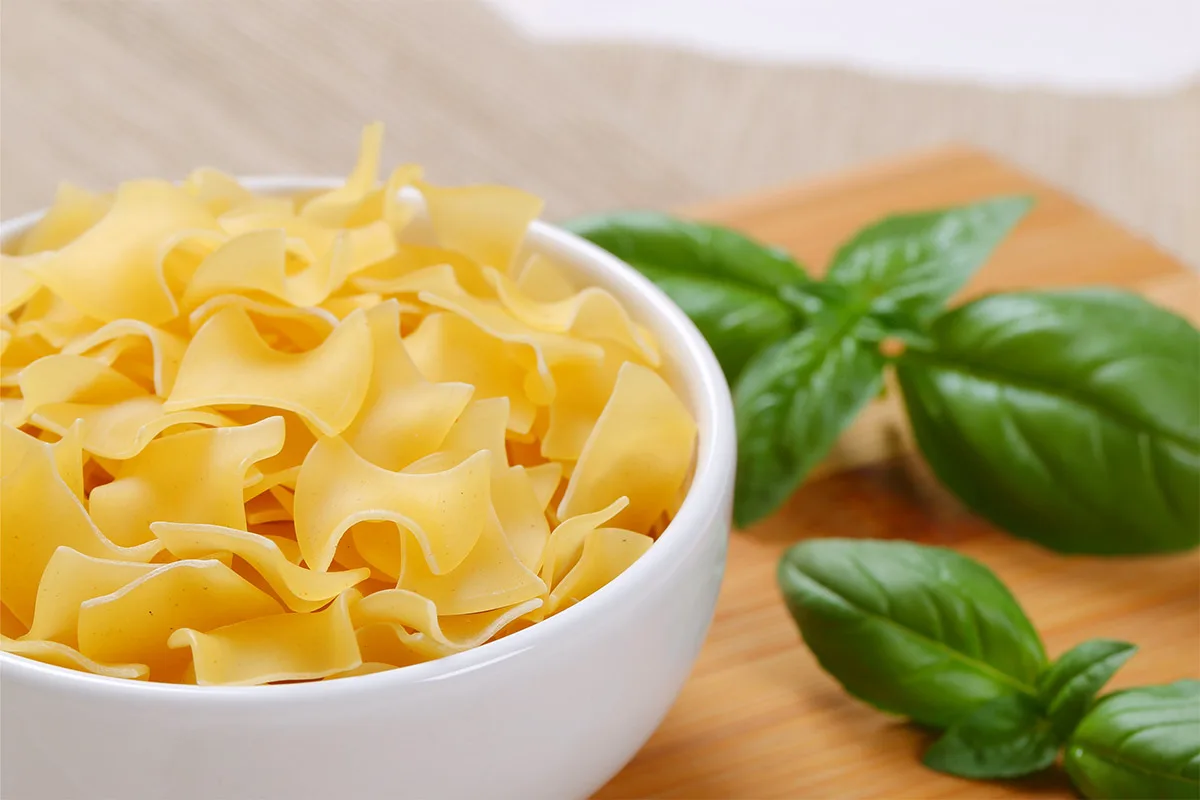 Quadretti pasta in a white bowl with basil leaves next to it | Girl Meets Food